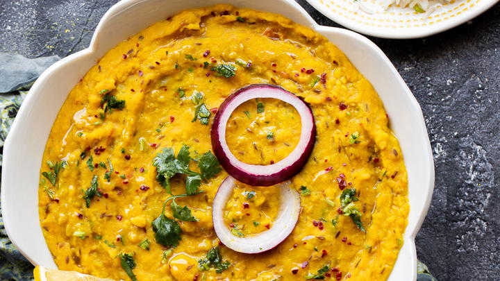 moong dal in a white bowl garnished with raw red onion and cilantro with a side of rice and naan