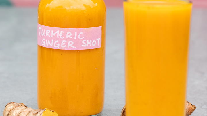Ginger Turmeric Shots, a poured glass in front of the bottle with some turmeric nearby