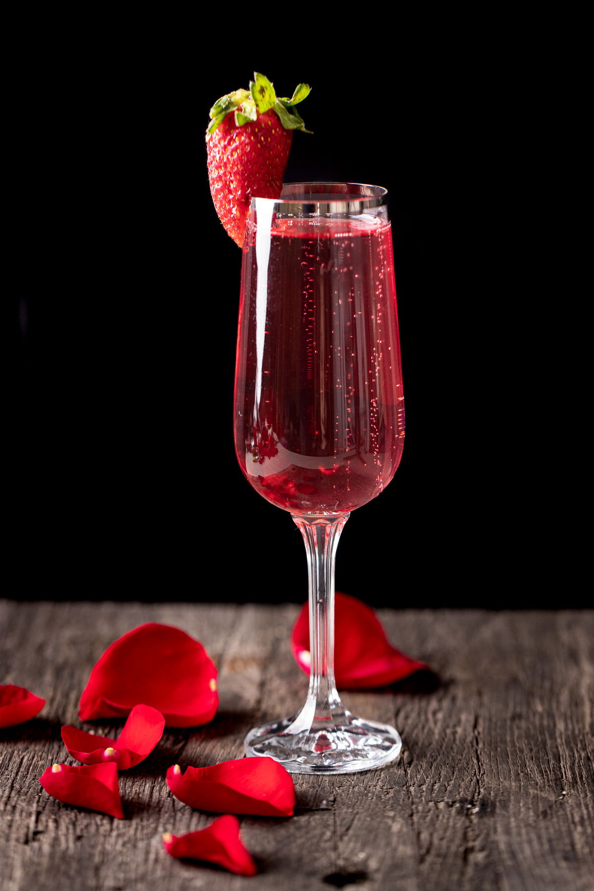 Rose mimosa garnished with a strawberry and decorated with rose petals.