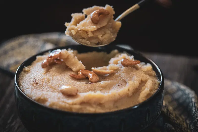 Spooning out some rava sheero from a bowl.