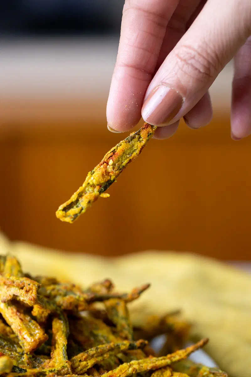 A hand holding a kurkuri bhindi