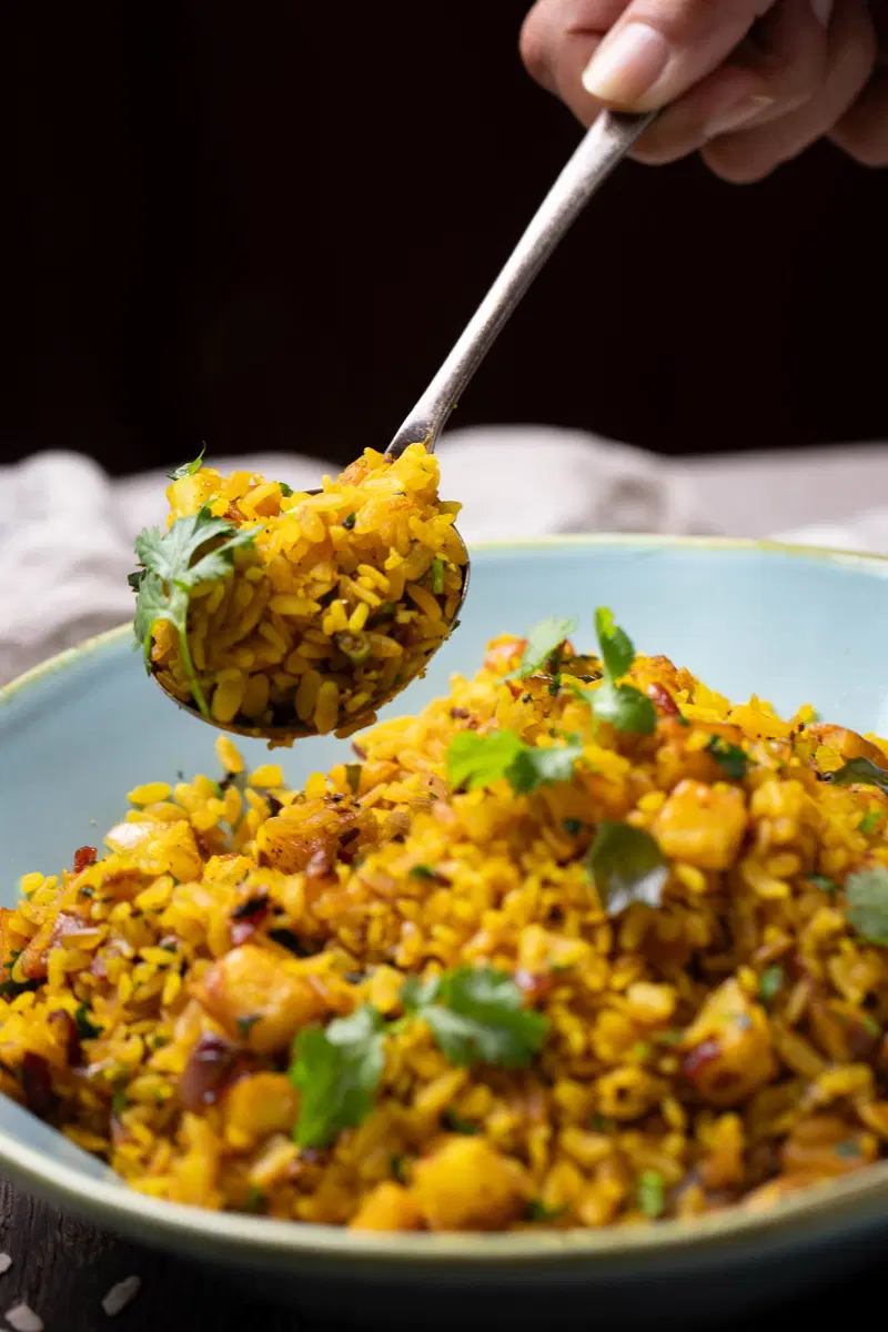 Spooning out some poha from a bowl.