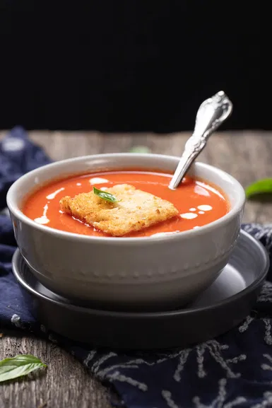 Side view of bowl of tomato soup with a piece of toast and basil
