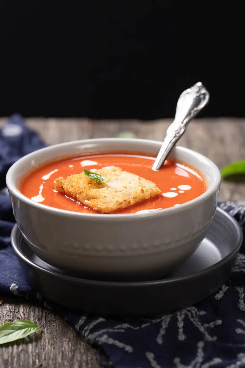 Side view of bowl of tomato soup with a piece of toast and basil