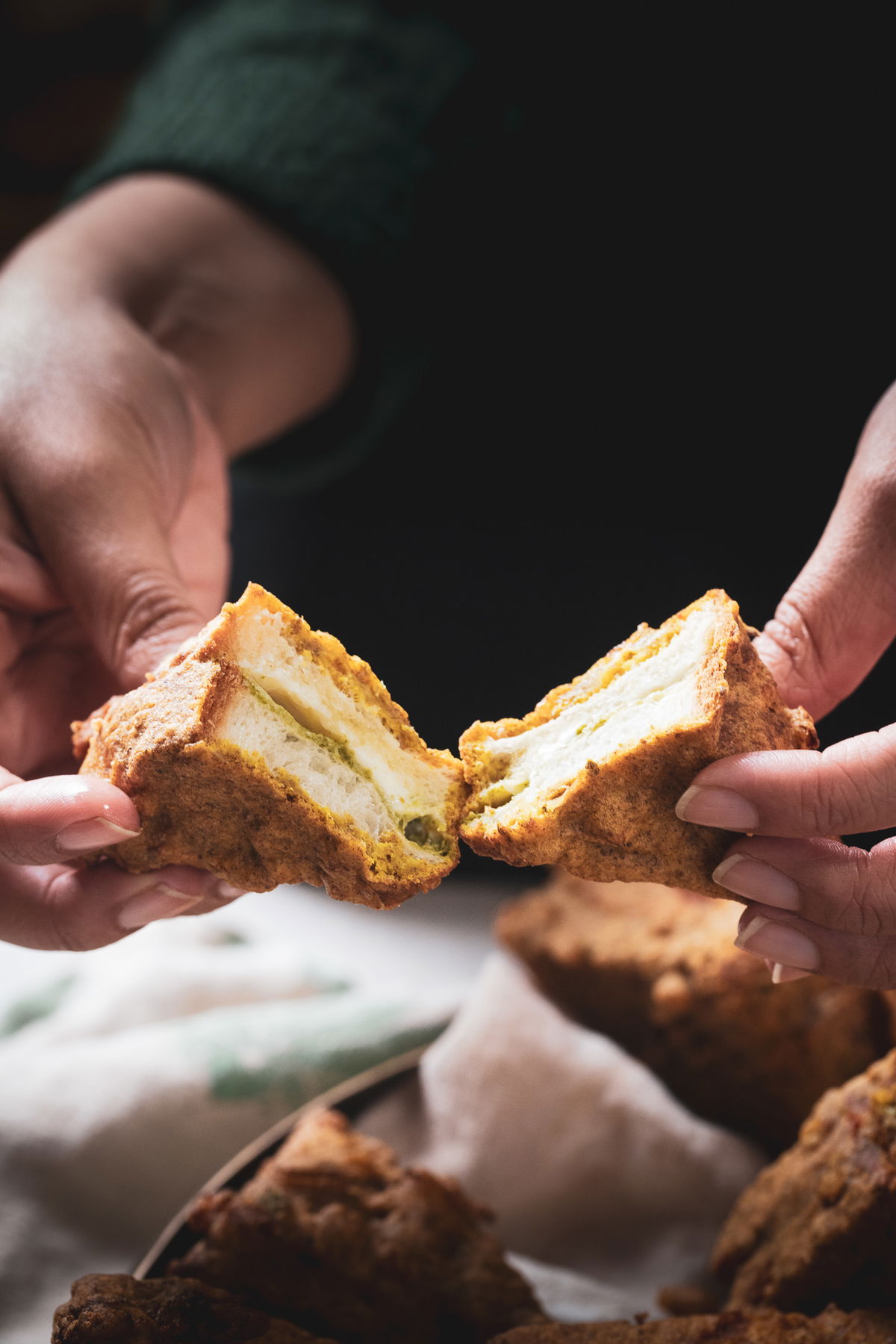 Holding the bread pakora, cut in half to show the inside layers.