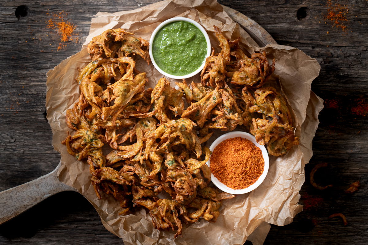 Kanda bhaji on a platter with cilantro chutney and garlic-red chili chutney.
