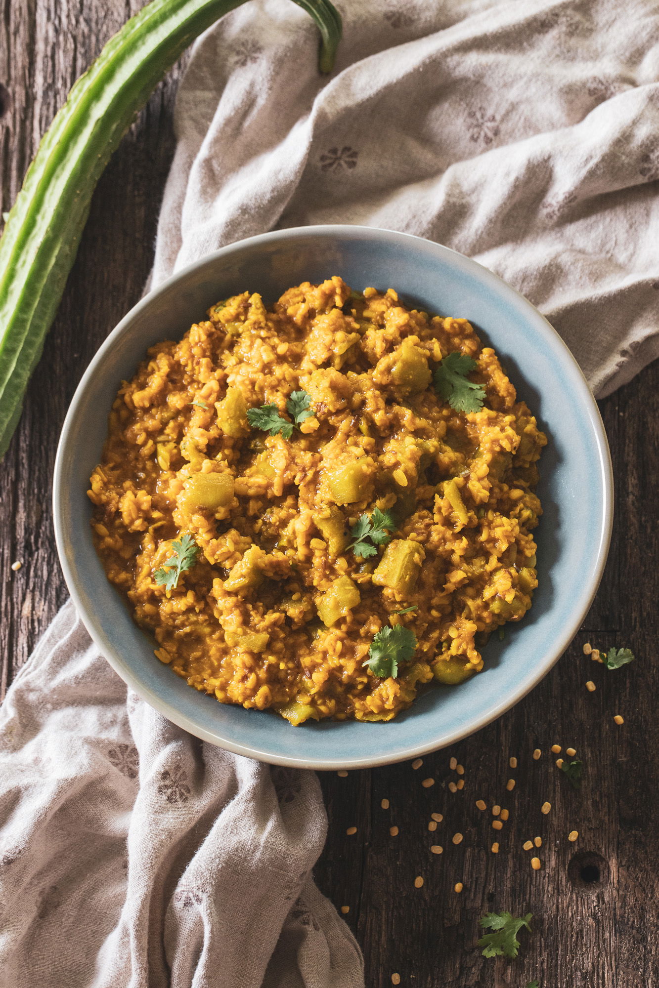Turiya mug ni dal nu shaak next to a whole, uncut ridge gourd